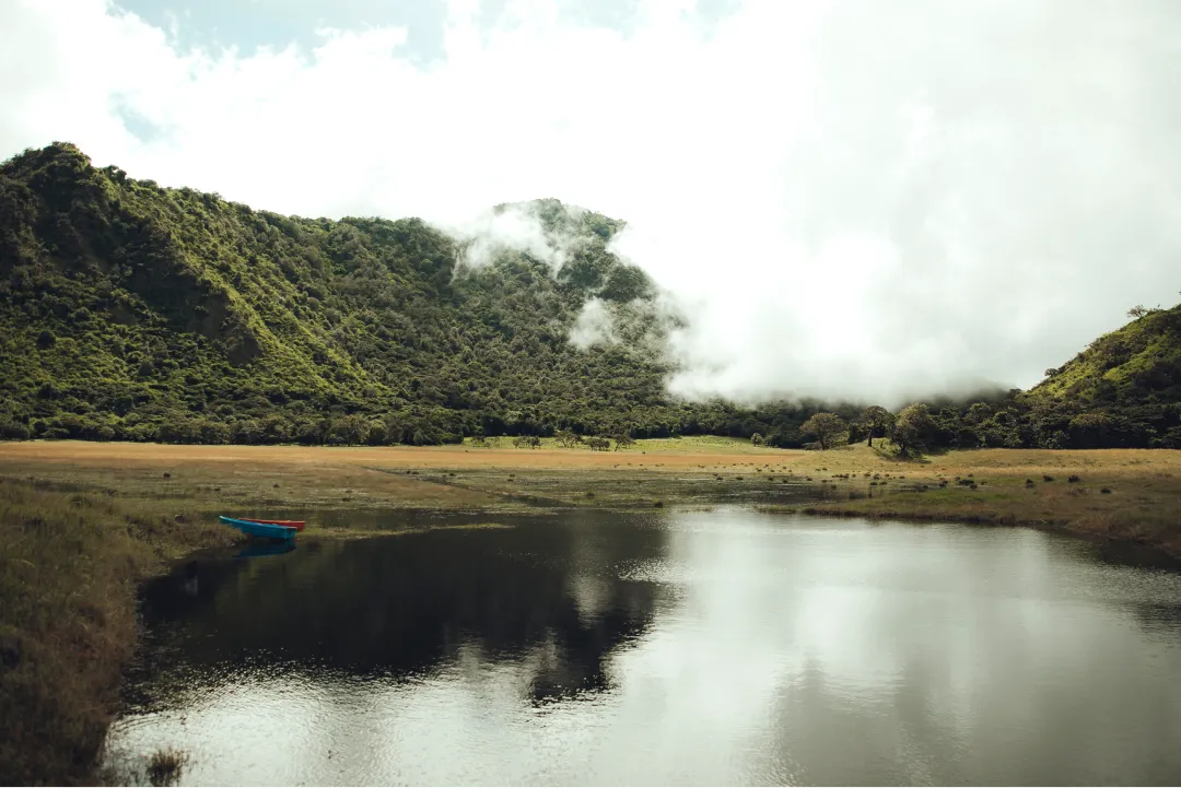 A small lake with a coffee mountain and rolling clouds in the background